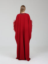 Load image into Gallery viewer, A model viewed from behind wearing a long, flowing red gown with feathered sleeves and a beaded neckline, set against a plain light gray studio background.
