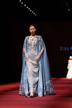 Load image into Gallery viewer, Model walking on a runway wearing a light blue evening gown with a cape.
